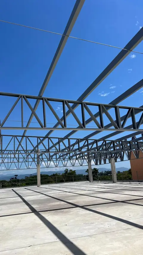 Estrutura metálica de uma obra industrial em estágio de montagem da cobertura, com vigas de aço sobre piso de concreto.