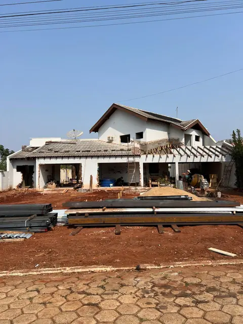 Obra residencial de alvenaria em estágio de construção, com estrutura principal erguida e telhado em fase de acabamento.